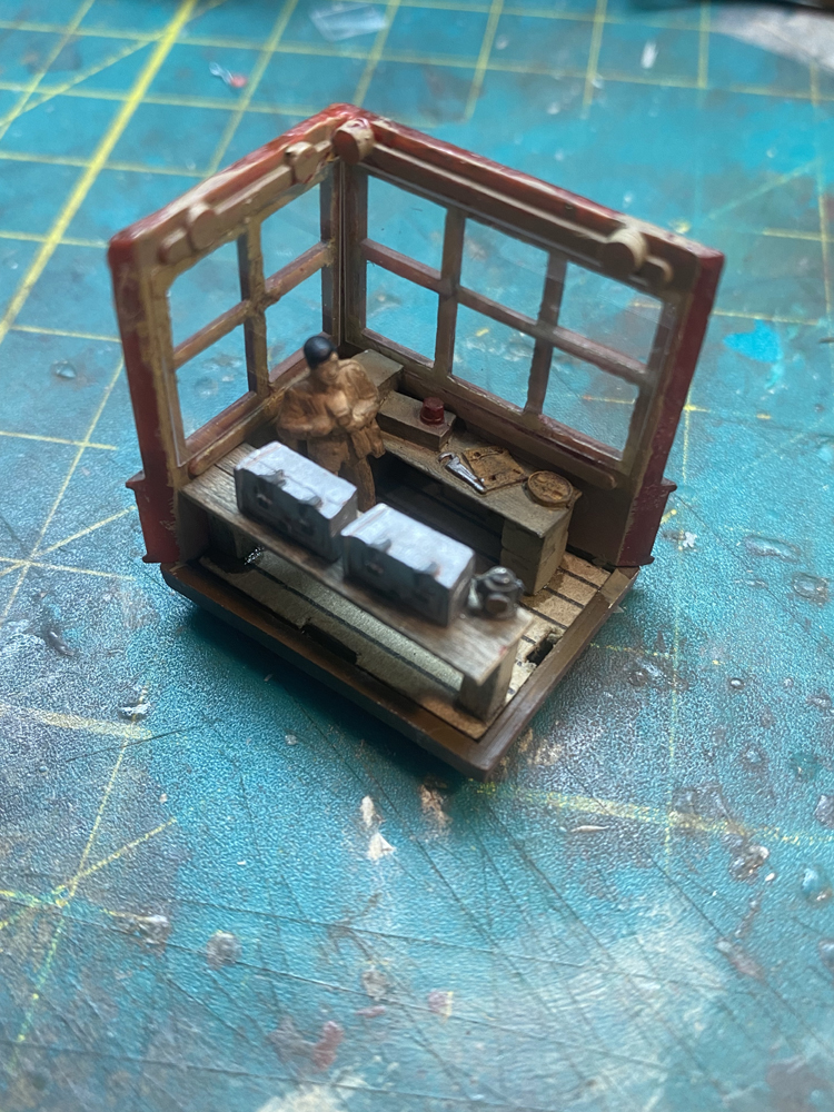 Model railroad tower with two walls removed showing detailed interior, including benches, tools, and a figure of a man with brown coat and dark hair.