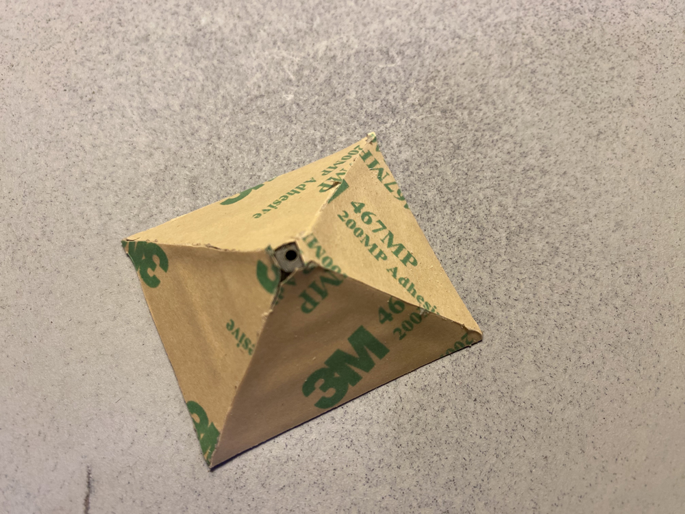 Model railroad tower roof covered in brown paper resting on a gray speckled workbench.