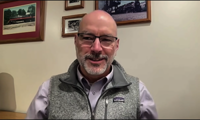 Man in vest with pictures on wall behind him. Trains LIVE — Rail news analysis with Bill Stephens