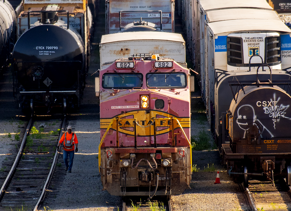 Front view of red and silver locomotive with remote-control operator walking beside