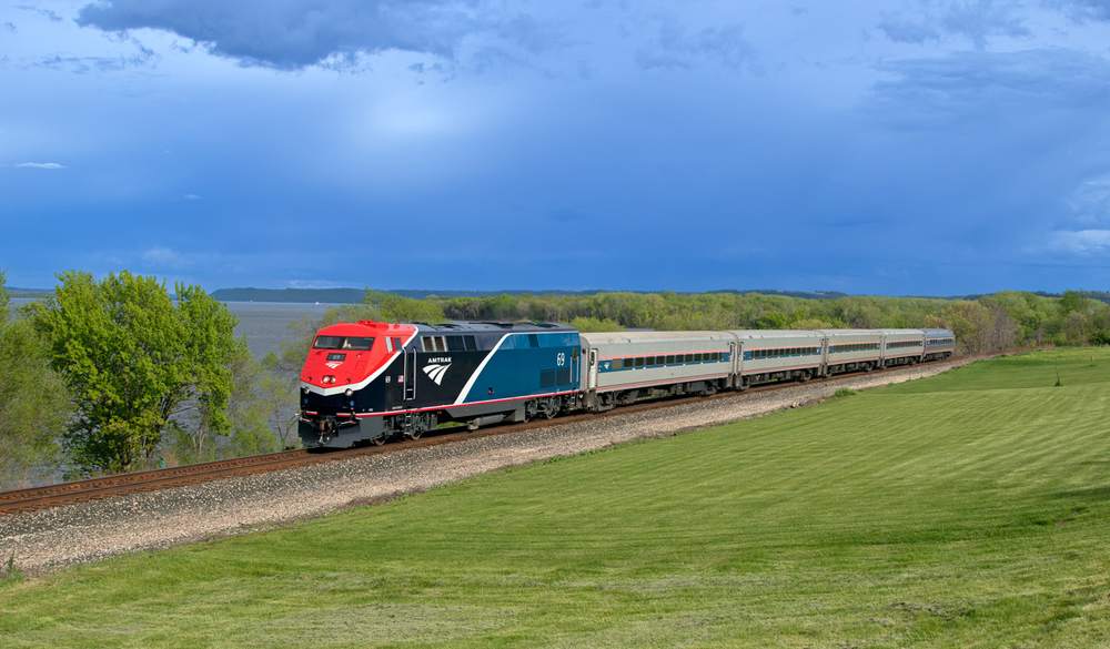 Passenger train next to lake under dramatic dark clouds