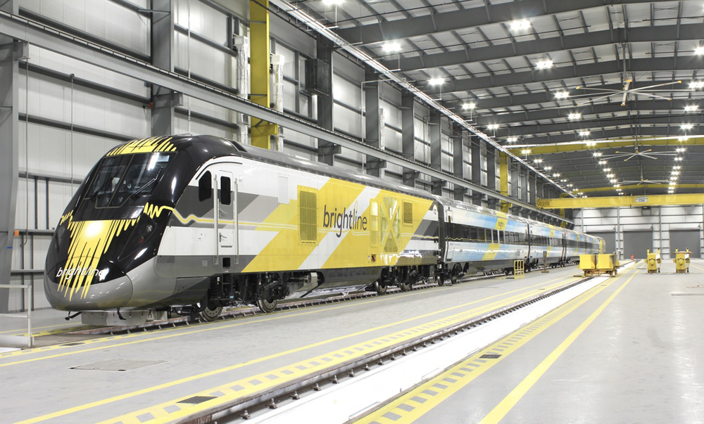 Train with yellow and white locomotive and blue and white cars in shop building