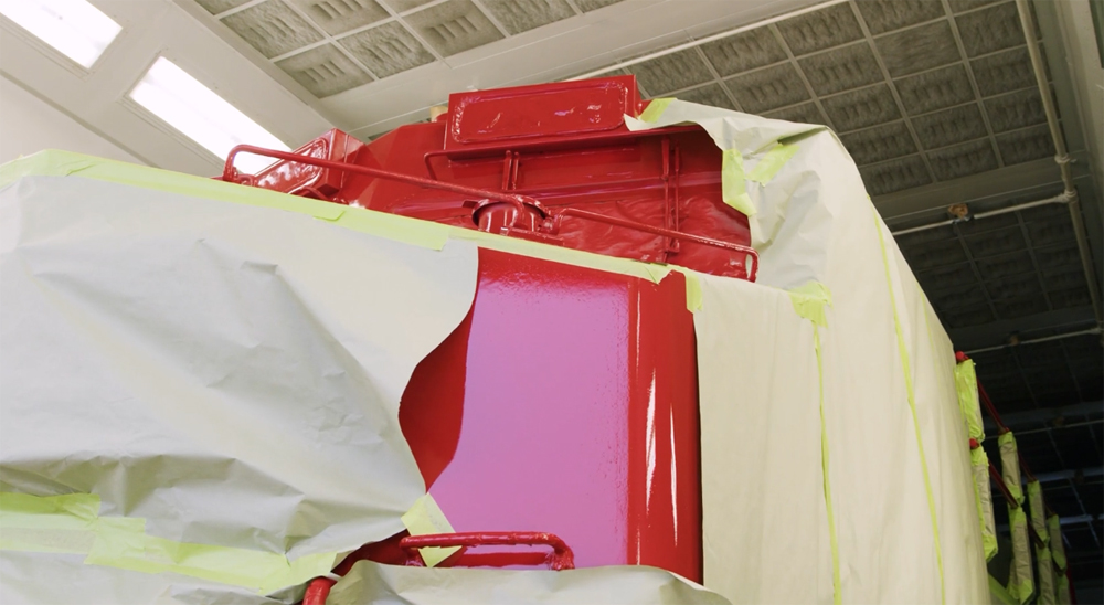 View of red paint on partially masked locomotive in shop