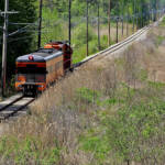 Locomotive and single passenger car on undulating straight track passing through field
