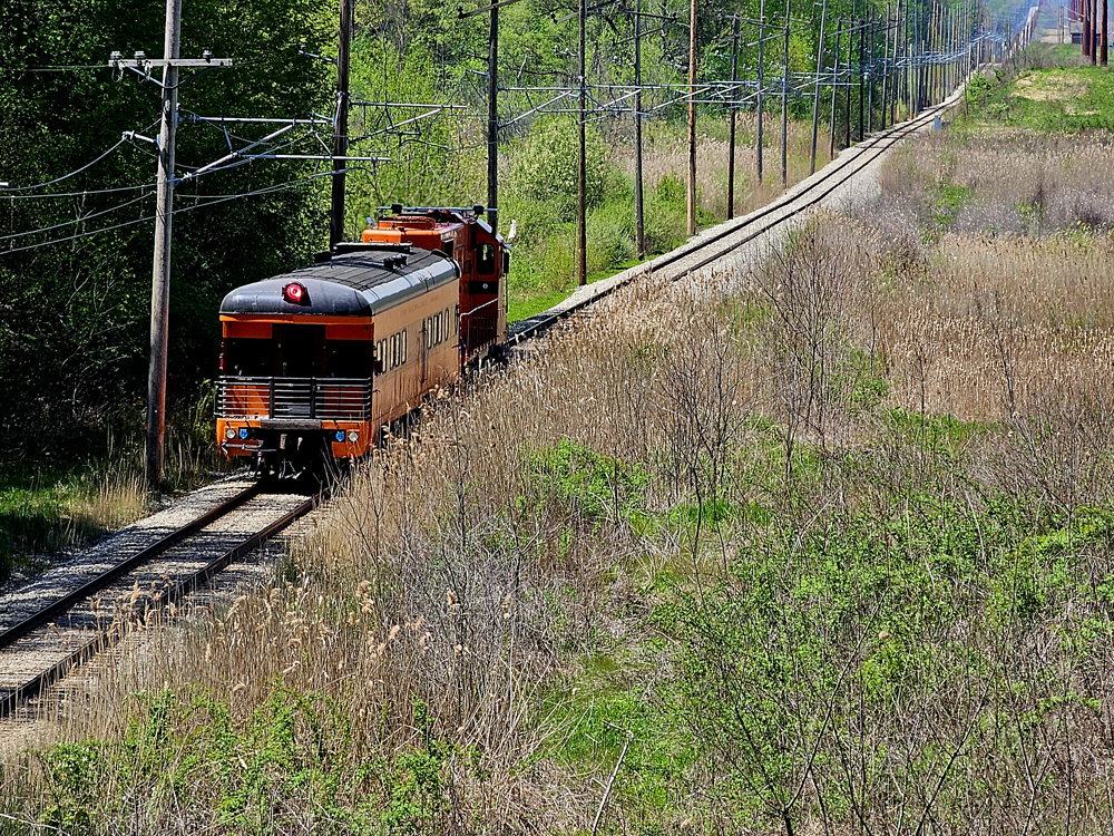Locomotive and single passenger car on undulating straight track passing through field