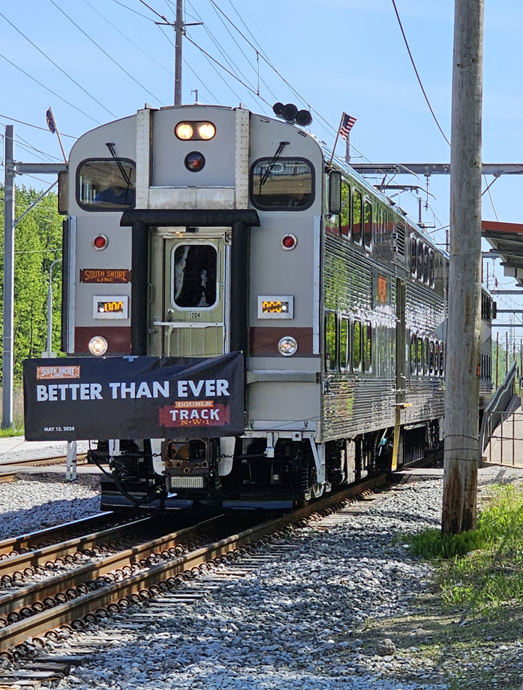 Bilevel electric train approaches banner strumng across tracks