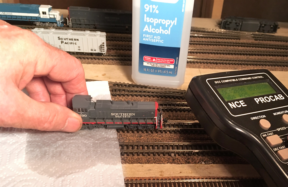 A hand holds a model locomotive so its wheels can spin on a dampened paper towel laid across a track