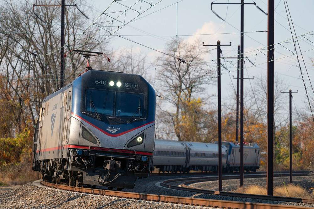 Amtrak train on curved track with tall poles