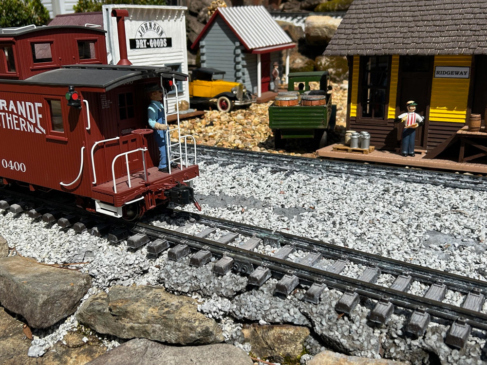 red caboose next to house and depot on garden railway