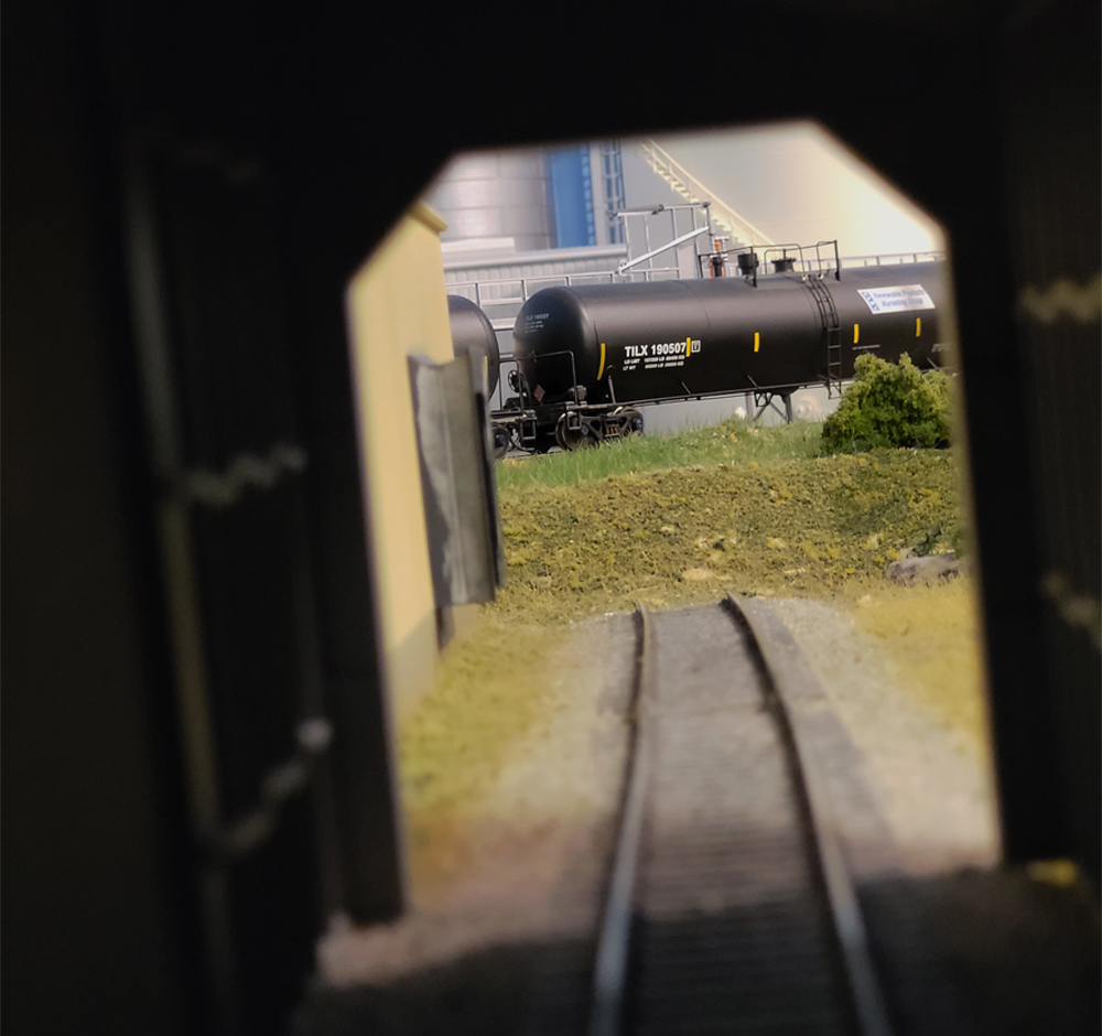 A tank car is seen through the end of a tunnel on a model railroad layout.