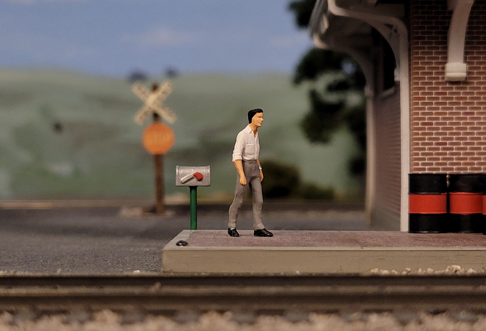 Model railroad cellphone photography tips: A figure on a model railroad layout approaches a passenger station.