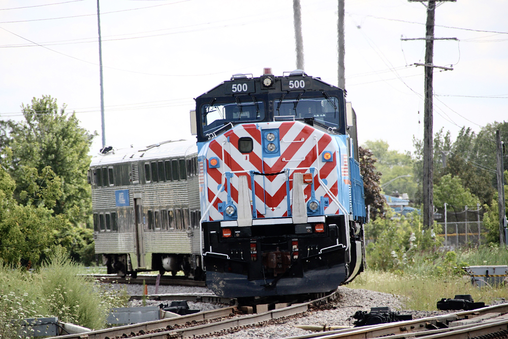 Blue locomotive with red and white nose striipes pushing train