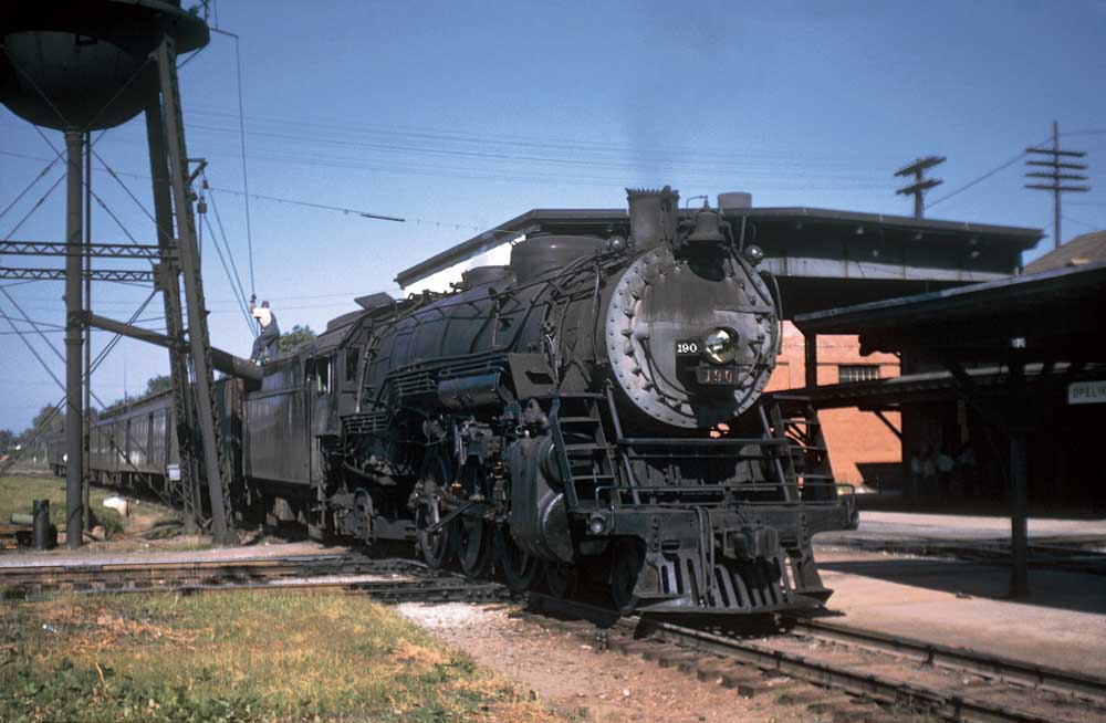 Steam locomotive with passenger train by water tank on crossing railroad track