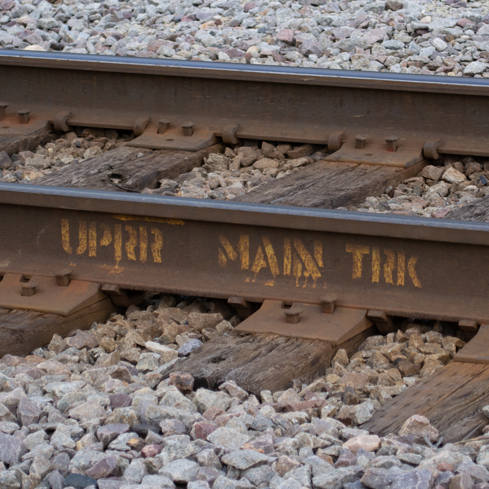 Color photo of railroad track with yellow stencil on web of rail.