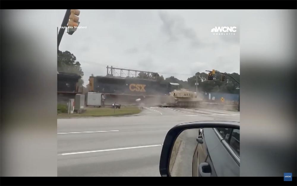 Screenshot of video showing train hitting truck carrying tan military equipment