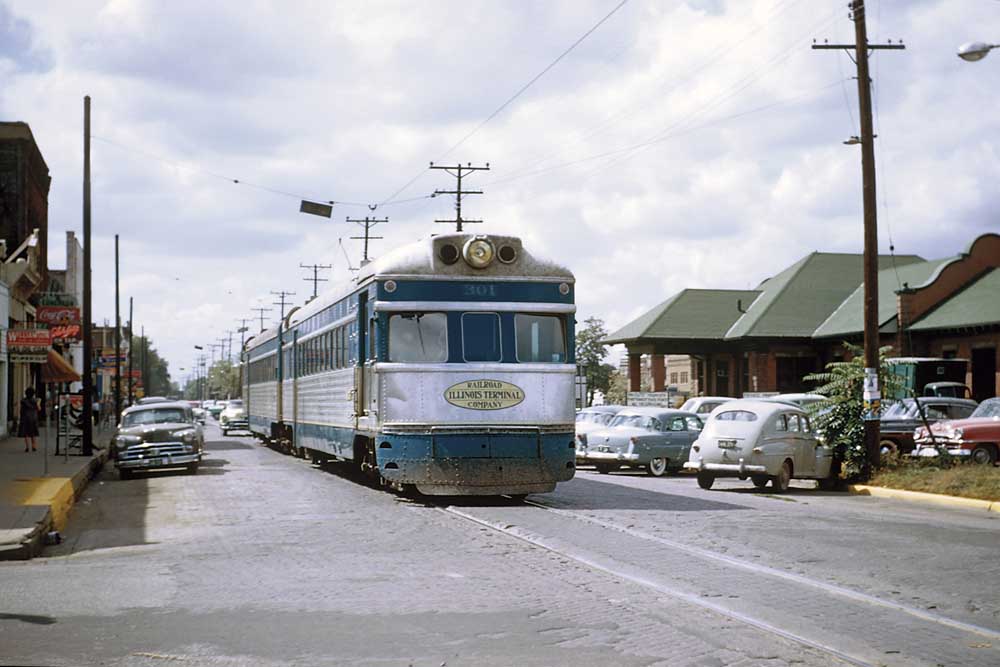 Electric interurban car in stainless-and-blue on street trackage