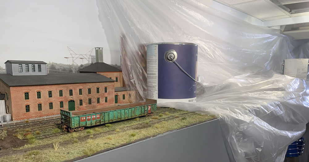 A model railroad layout with a plastic cover weighted down with a paint can