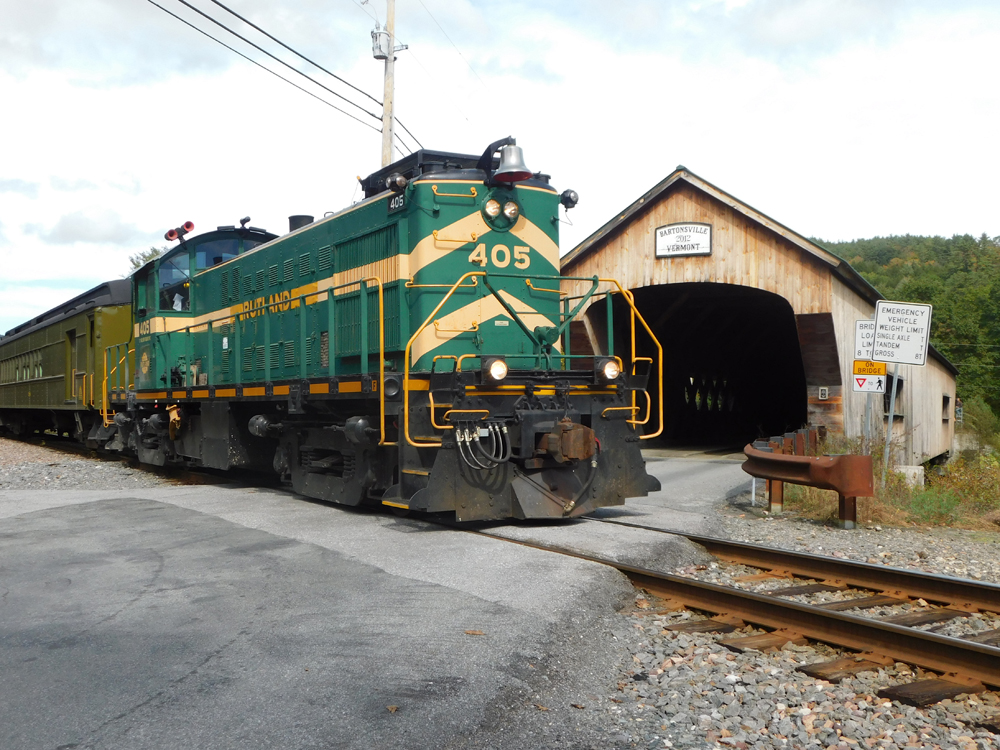 green and yellow locomotive in front of covered bridge
