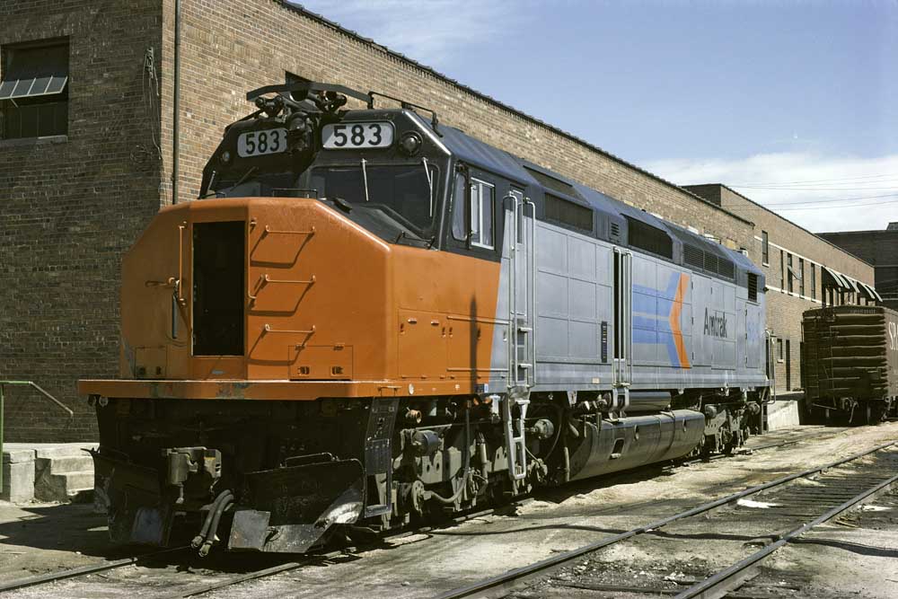 Silver Amtrak SDP40F diesel locomotives with red noses sit outside brick building