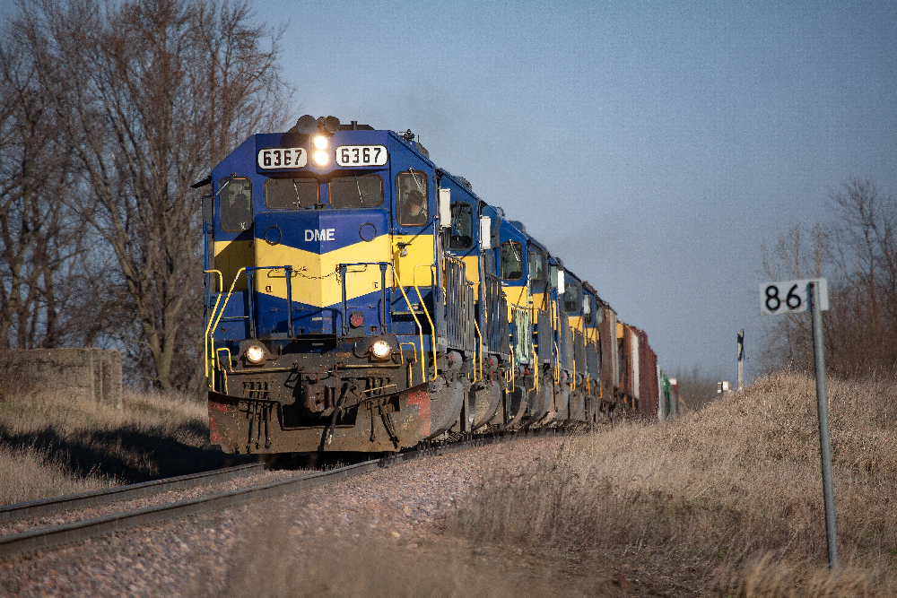 Blue and yellow diesel locomotives lead a freight train. Smoking Dakota, Minnesota & Eastern Railroad