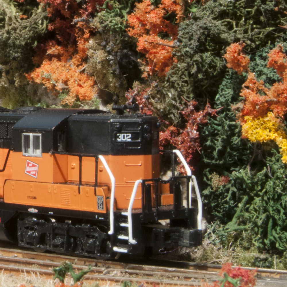 Color photo of Z scale Milwaukee Road EMD GP9s emerging from tunnel in a scene with fall foliage.