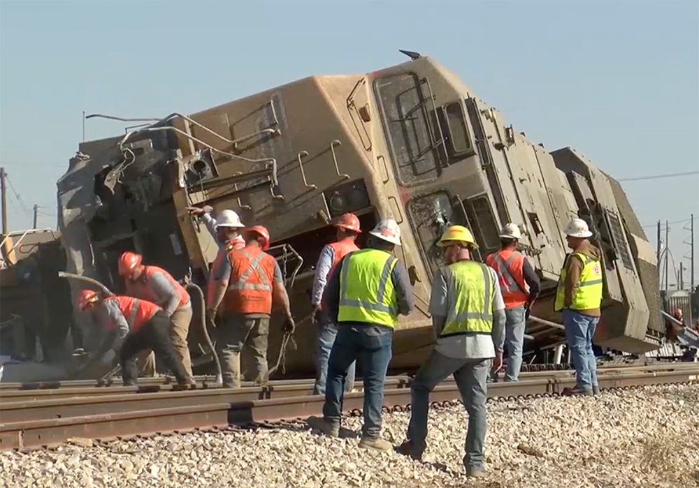 Damaged locomotive on its side surrounded by workers