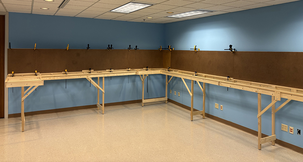 A large room with tan floor and blue walls with wood benches built along two of the walls and featuring dark-brown vertical panels. This room will eventually be home to the East Troy Industrial Park RR in HO scale.