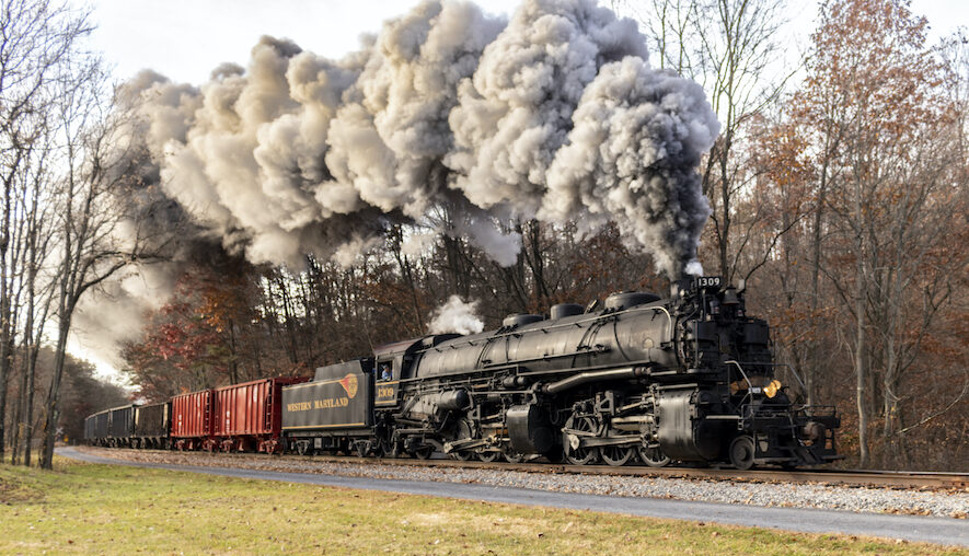 A color photograph of a steam locomotive and tender leading a passenger train