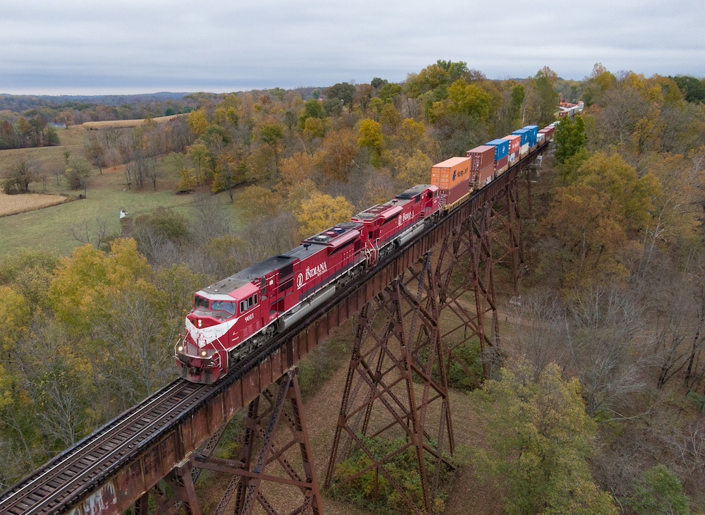 Red locomotives cross a bridge with a freight train