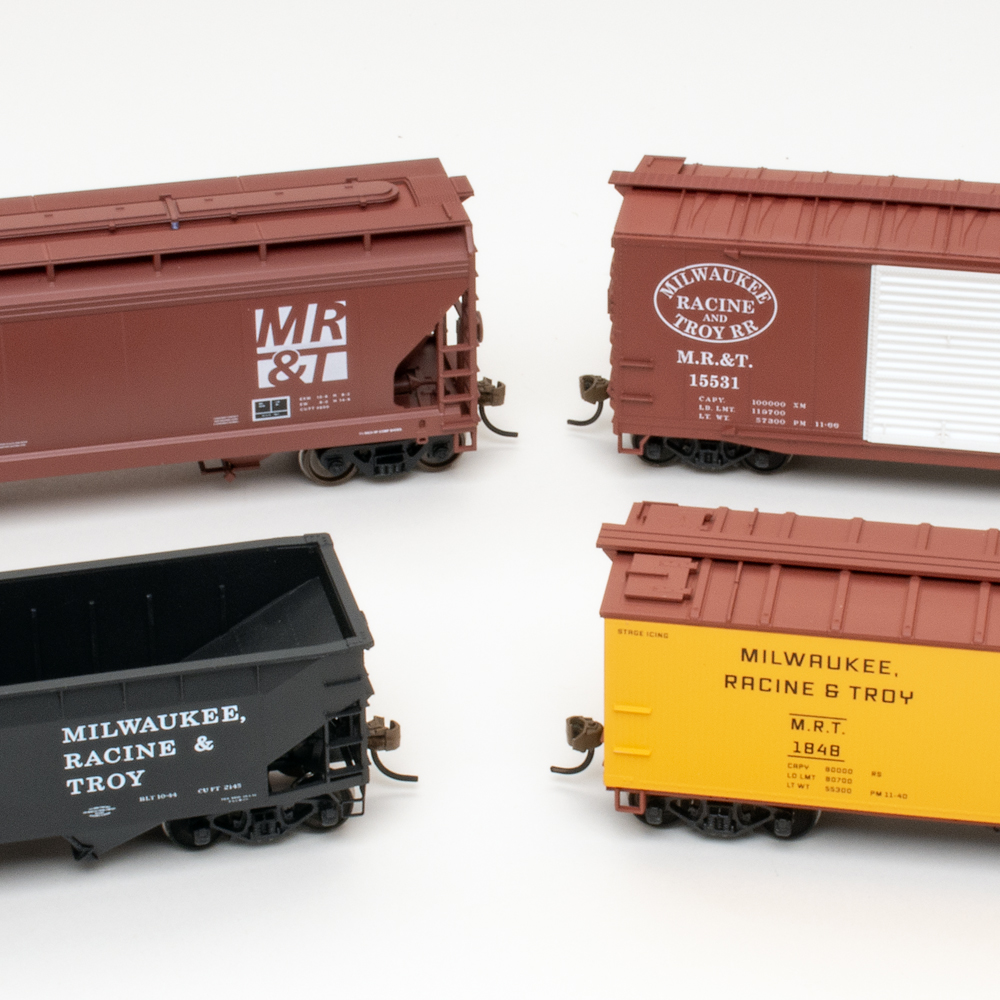 Color image of four HO scale freight cars in brown, black, and yellow paint on white background.