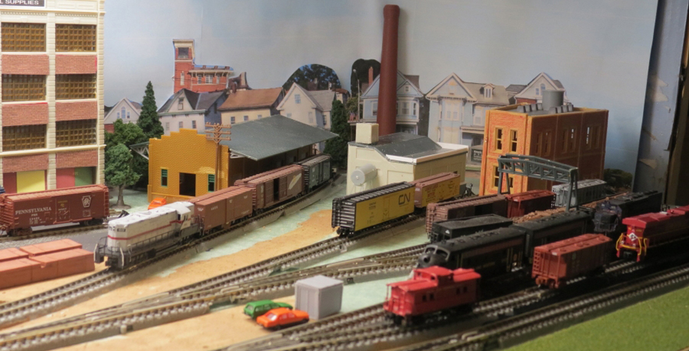 Multiple model trains sit in a switching yard on a model railroad layout