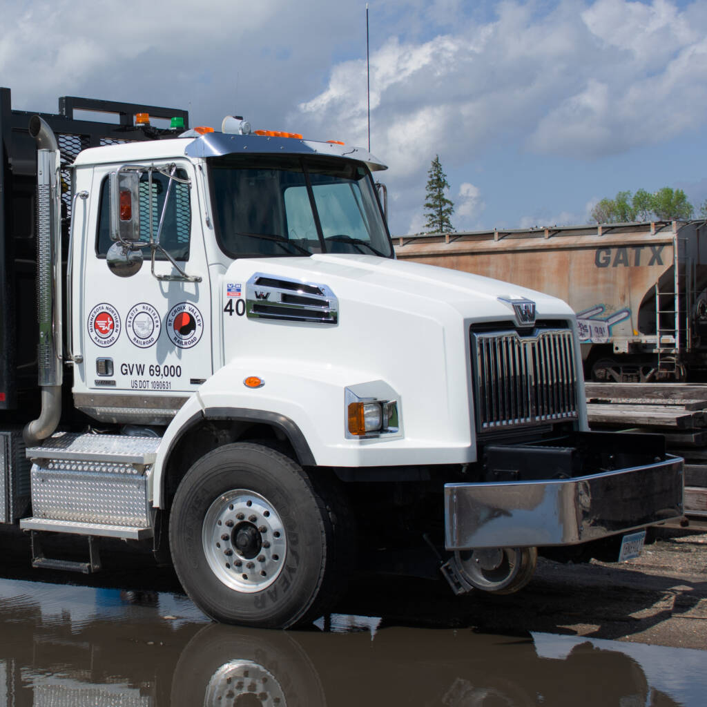Color photo of white truck with black bed and yellow grapple