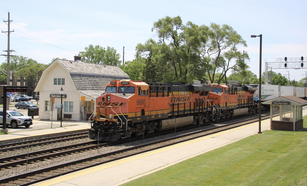 Orange locomotives pass barn-like commuter rail station