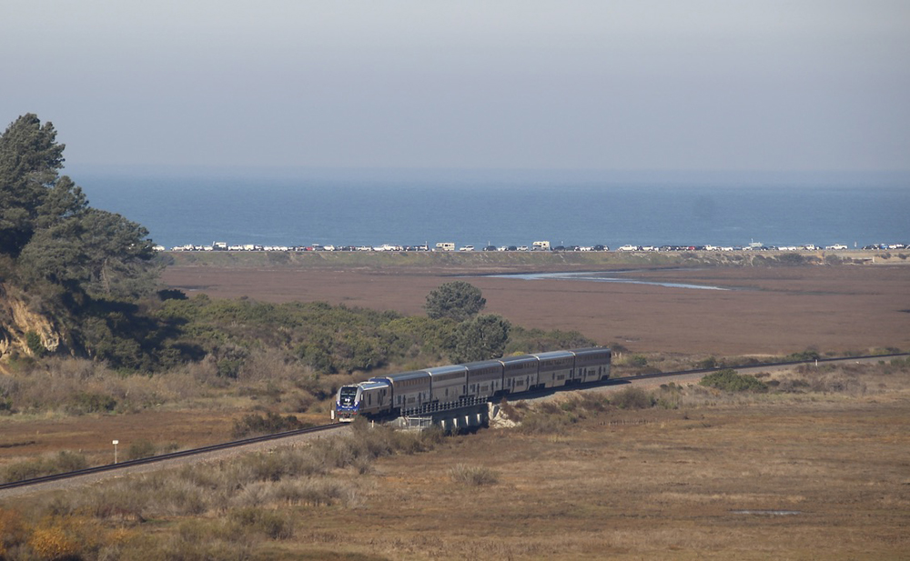 Passenger train crossing bridge with ocean in background