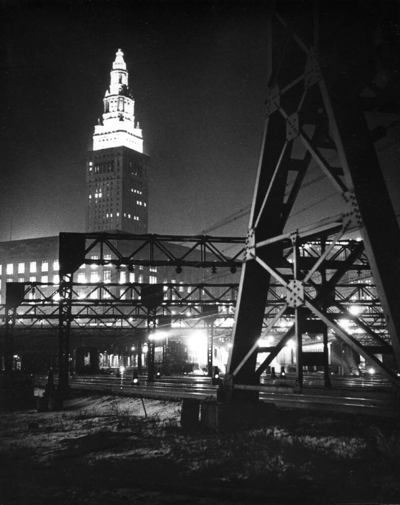 Tall building at night with electrified trains in foreground.