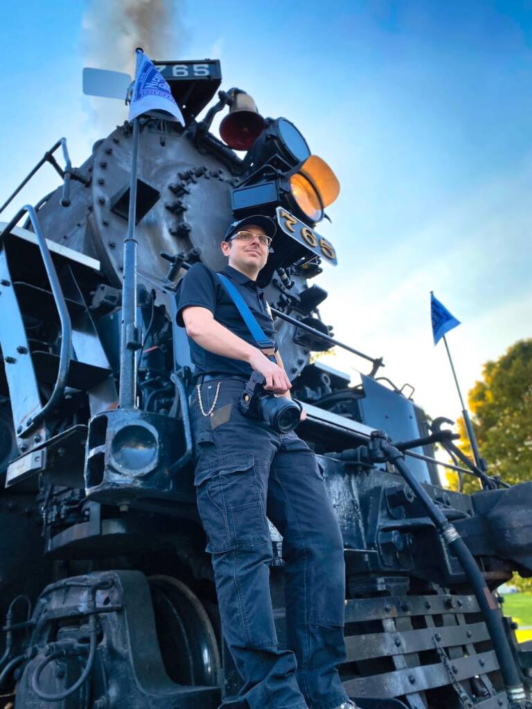 Young individual standing in front of a steam locomotive