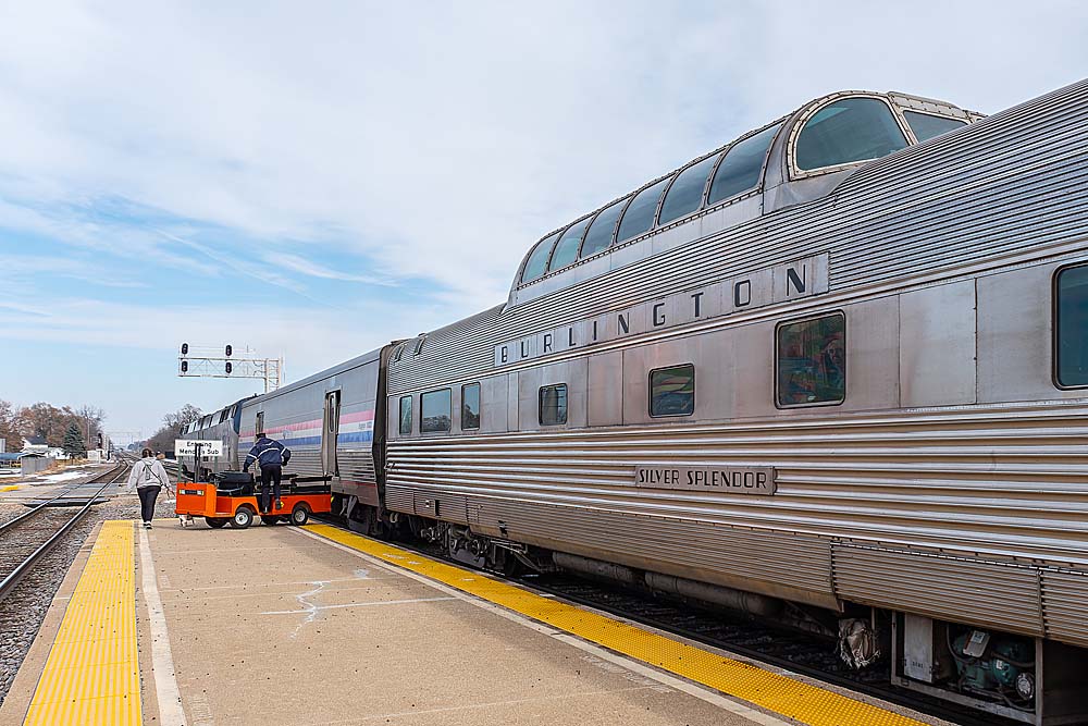 Glass-domed silver passenger rail car named Silver Splendor by station platform