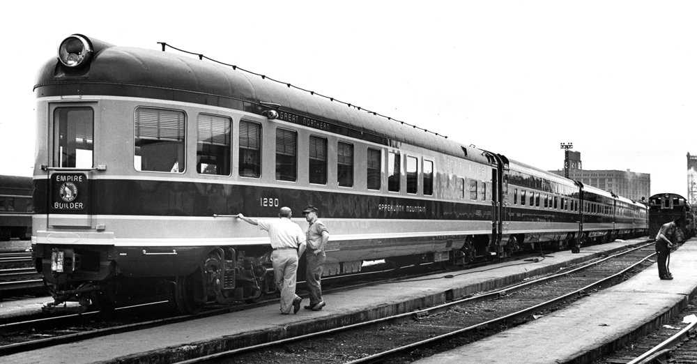 A black and white photograph of two men standing next to a passenger car