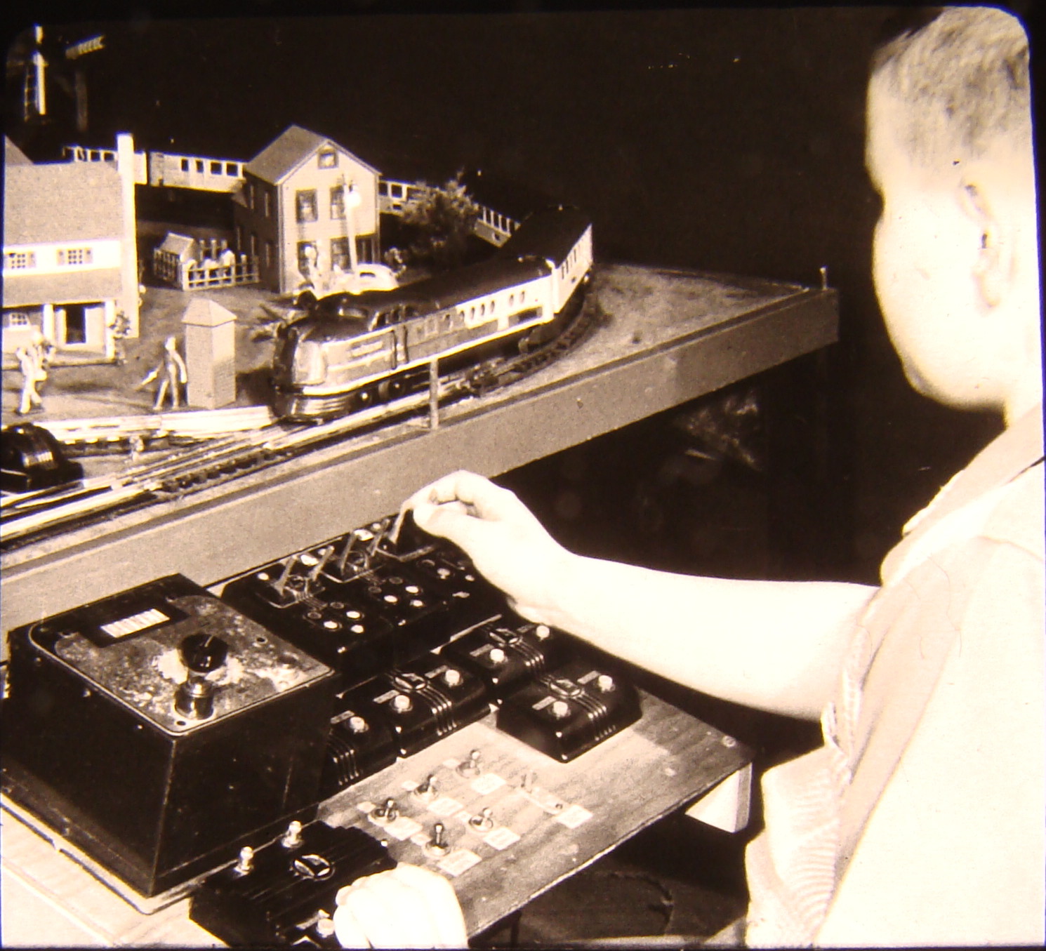 Black and white image with child near toy train layout
