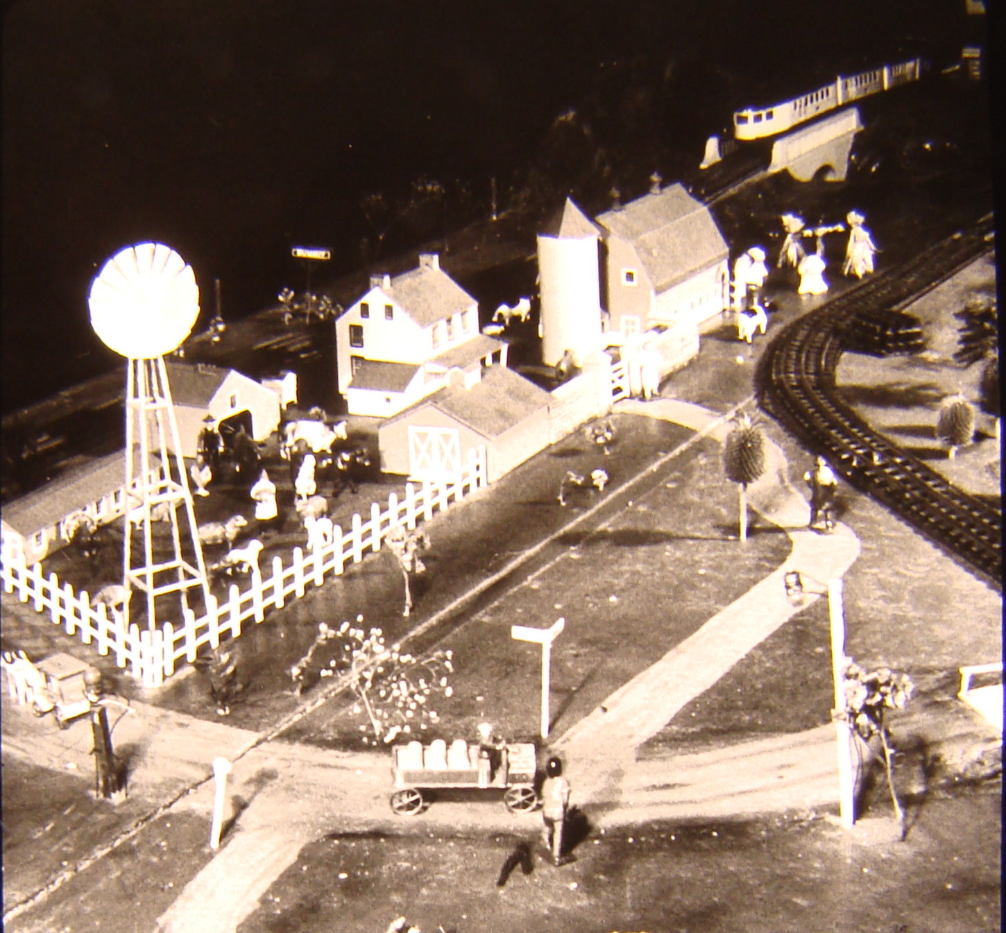 Black and white image on toy train layout with a house and cars