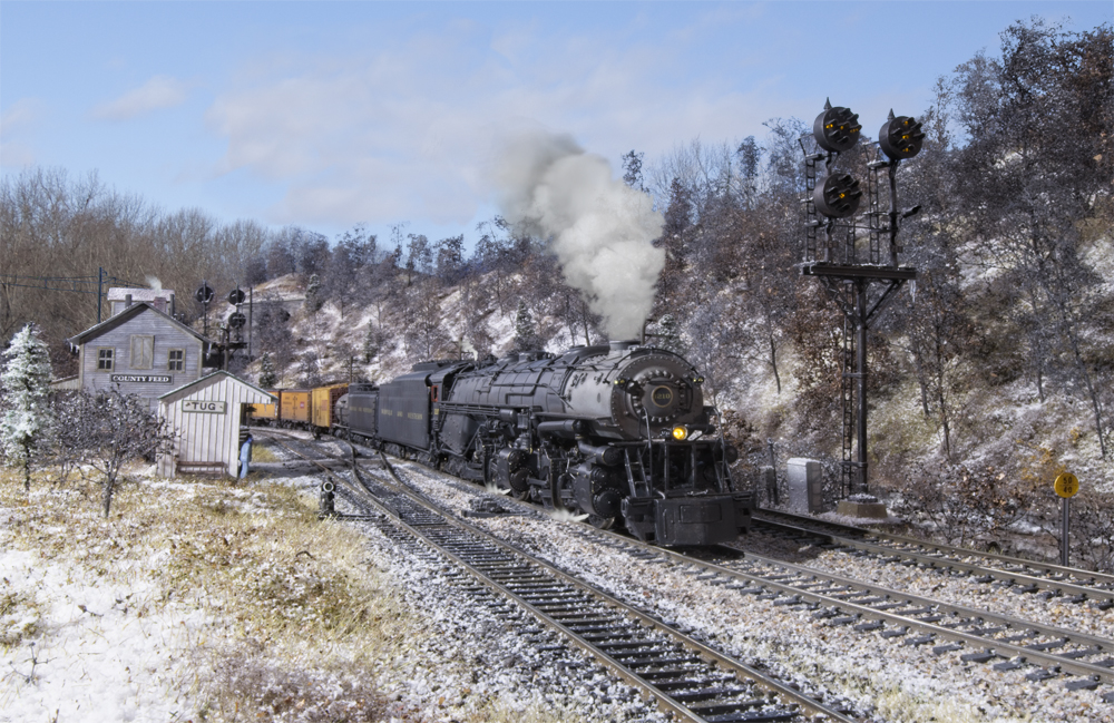 Color photo of steam engine pulling freight train through snow-covered scenery.