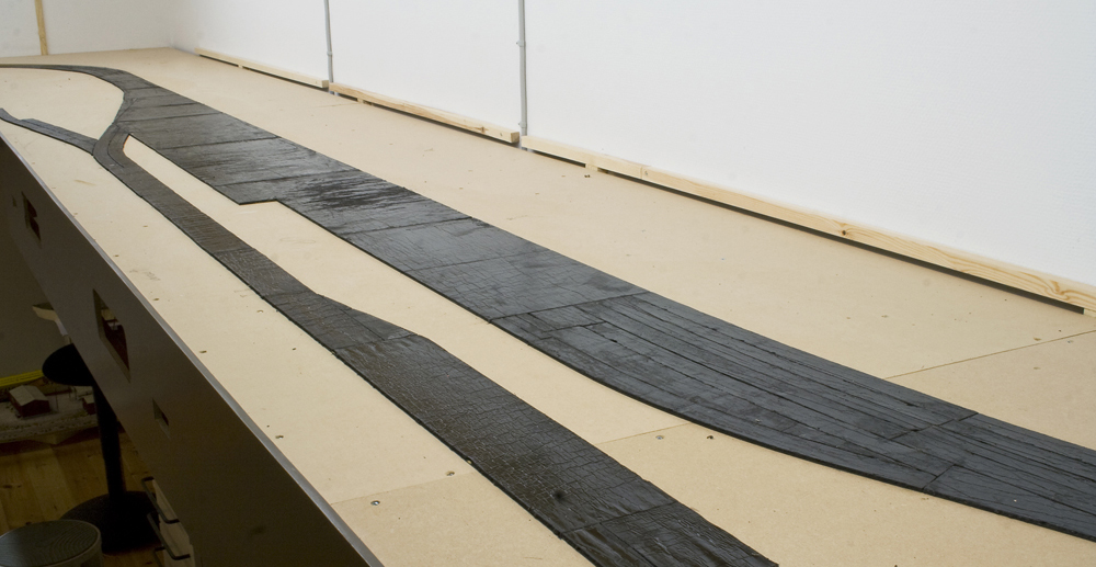 Color image showing sound-deadening material attached to medium density fiberboard layout surface.