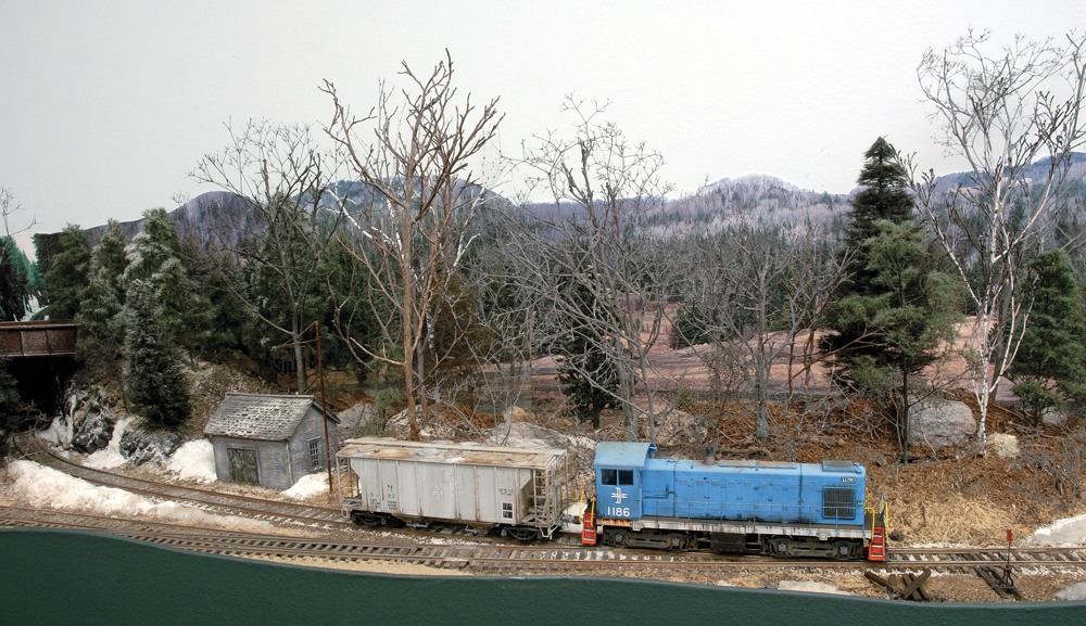 Color photo of switcher and covered hopper going through early spring scene.