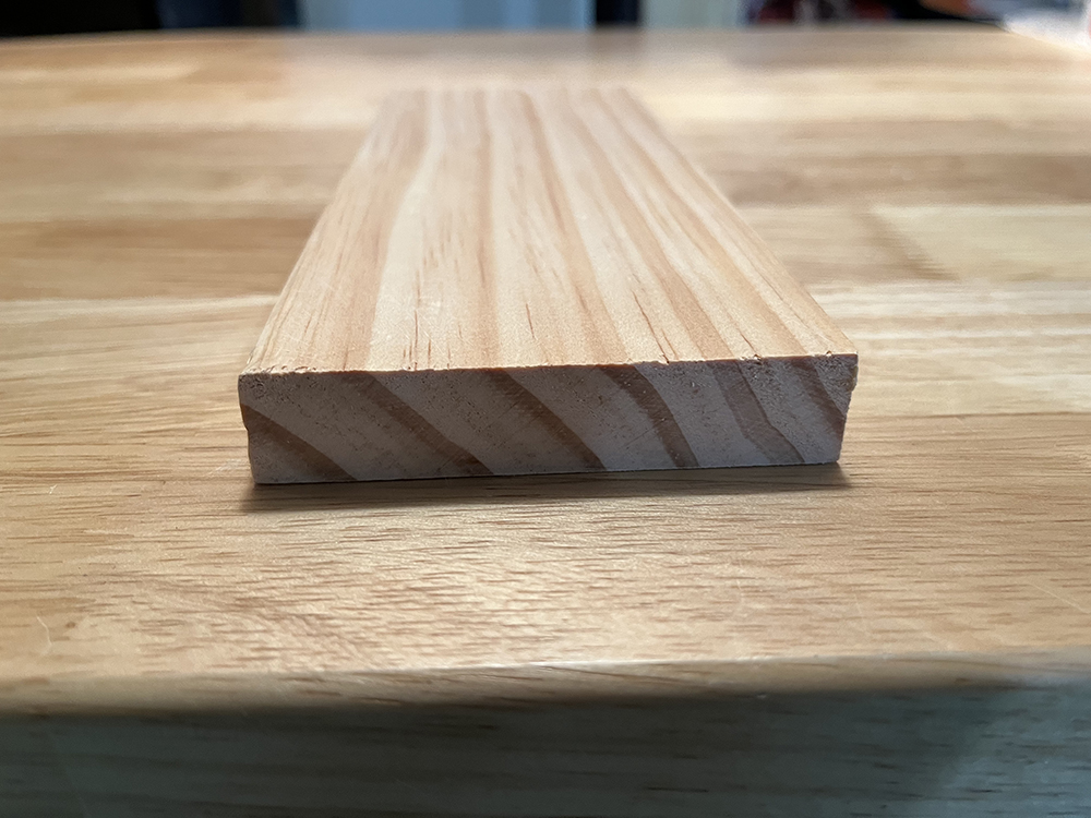 A tan piece of wood viewed from the end showing grain lines and a curve upward.