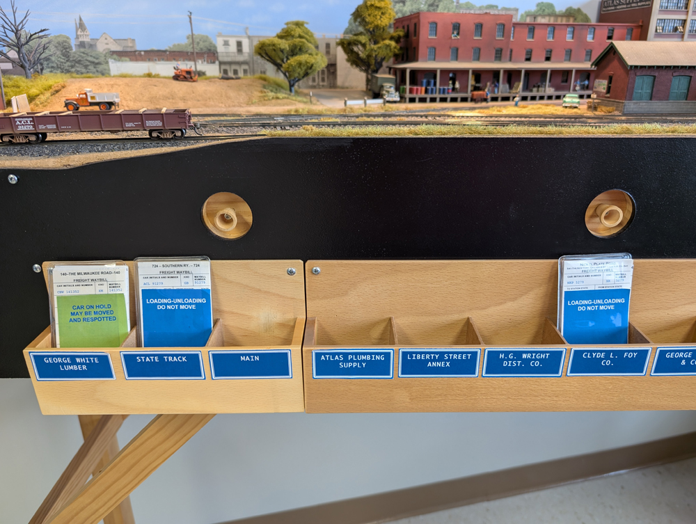 Model railroad car cards in their slots on the side of a train layout.