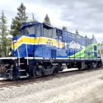 Blue, green, and yellow locomotive moving two freight cars