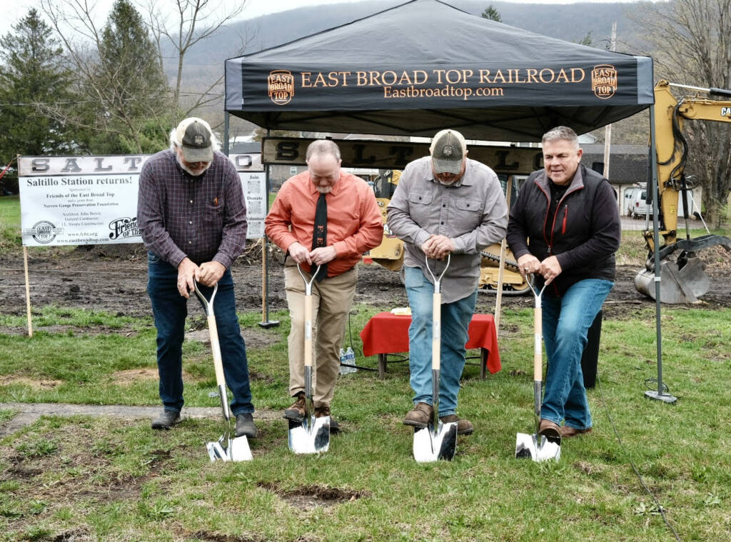 Four men digging into grass with shovels at groundbreaking event