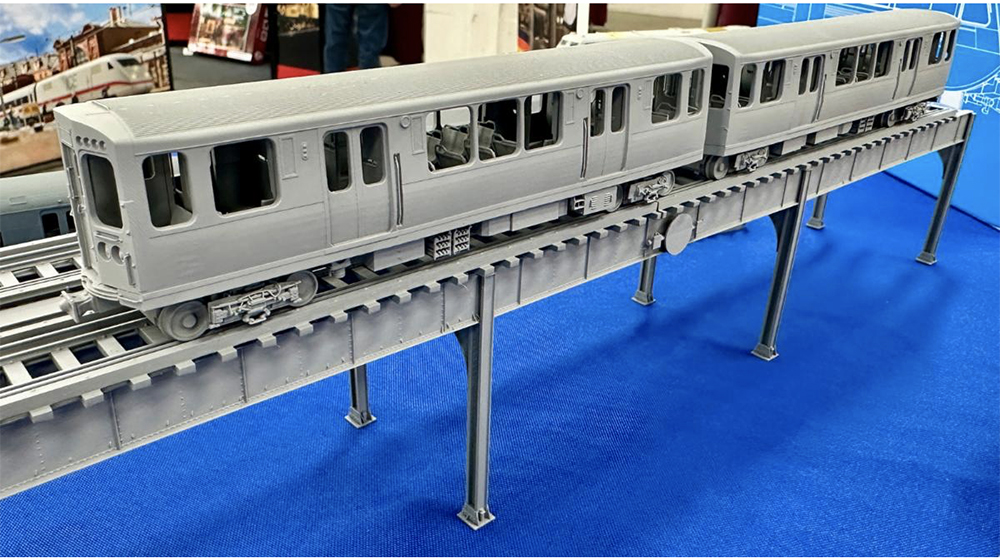 Model of a Chicago Transit Authority pair of elevated train passenger cars on a short section of elevated track made of gray plastic and resting on a table with a blue top.