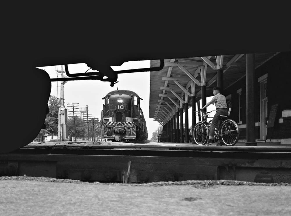 A boy on a bicycle watches a black locomotive