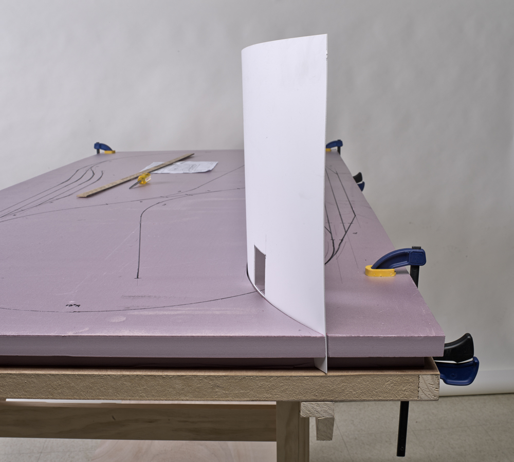 Color photo showing white styrene sheet used as backdrop on unfinished model railroad.
